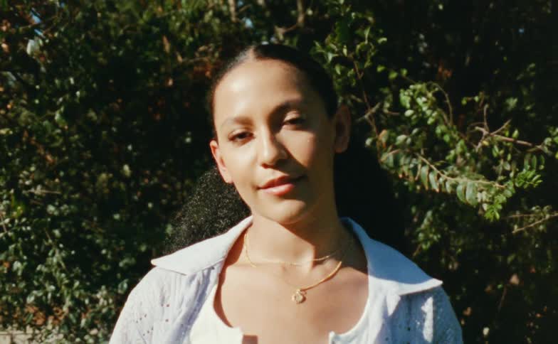 Close up of a young woman standing in front of a bush caught on vintage film looking at the camera