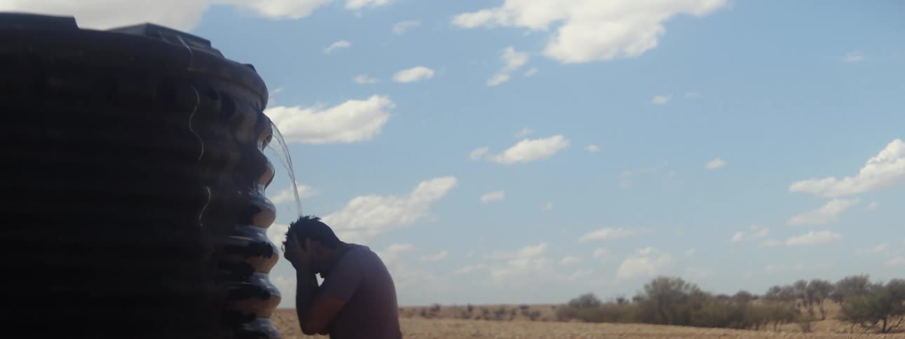 Man having an outdoor shower from water tank in the field