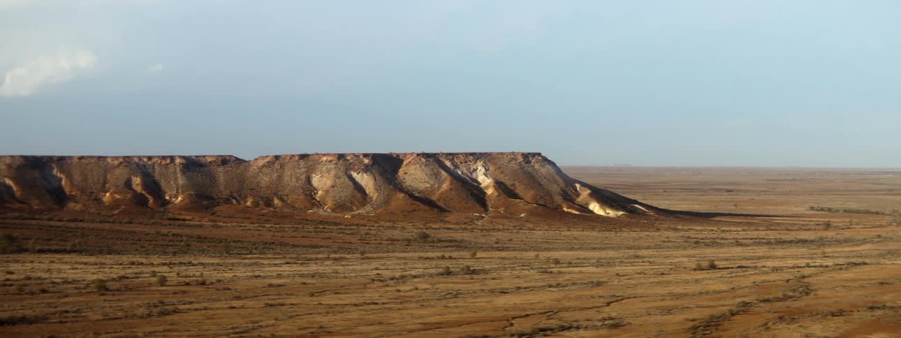 A landscape view of a desert with a large rock formation