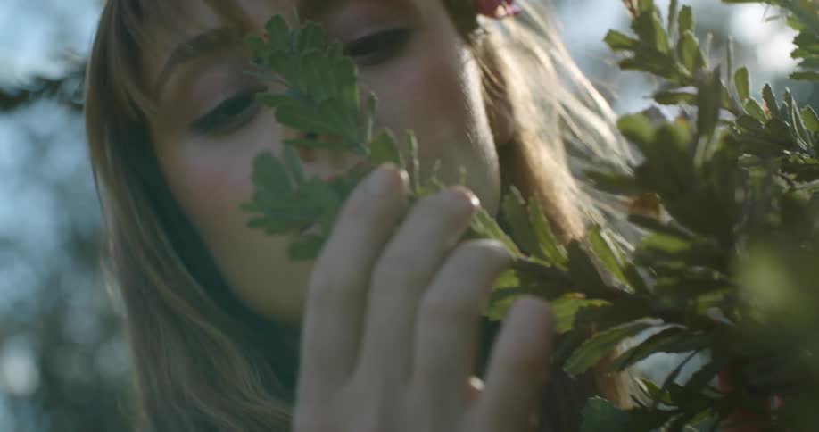 A woman with a pink flower in her hair lovingly caresses and touches a flowering branch