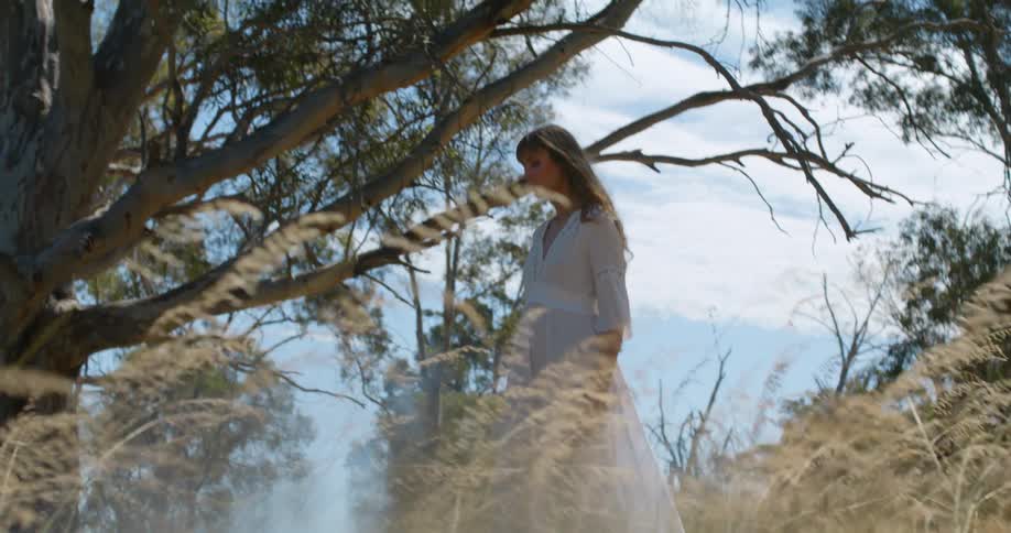 A woman walks under trees in a field