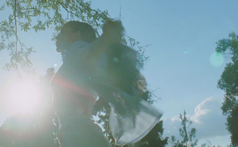 Sunlight shines behind the silhouette of a young woman dancing on a park at morning