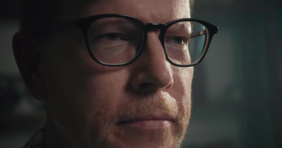 A man wearing glasses sits in a room