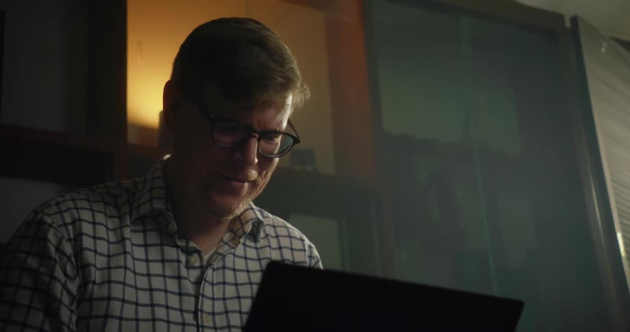 Man sits on couch smiling slightly while using laptop