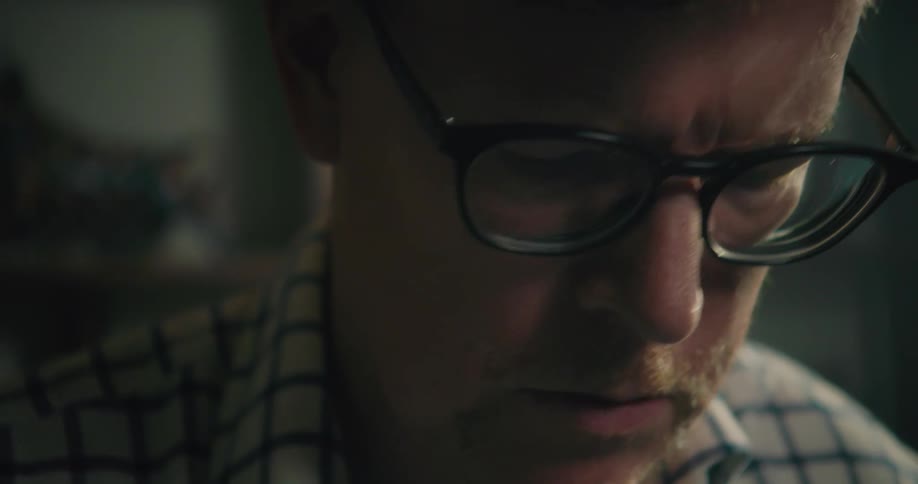 A man wearing glasses is looking down intensely at what he is working on doing