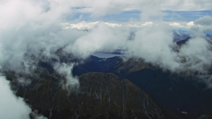 Flying through white clouds floating above mountain peaks and a blue lake
