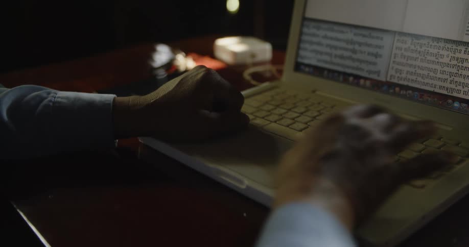 A man is sitting at a table typing on a laptop computer