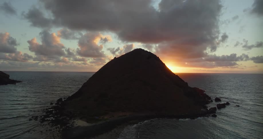 The sun shining on the ocean surface creating peaked rock silhouettes of small islands