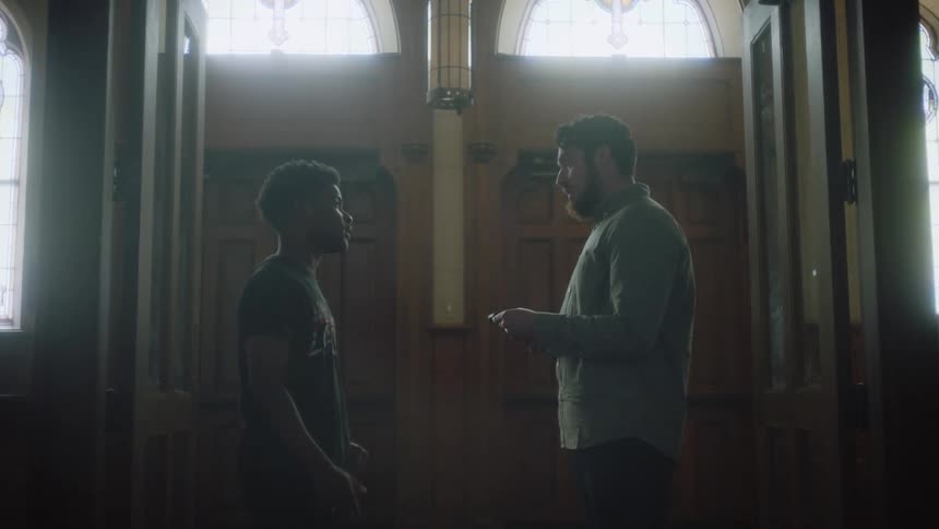 A man talks to a teenage boy as he keeps looking down at a cell phone