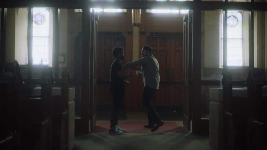 A man holds a cell phone and looks at it as he talks to a teenager in a church and then pats his back as he walks away