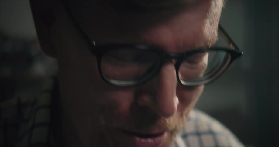 A man wearing glasses is looking down with a smile on his face as he talks