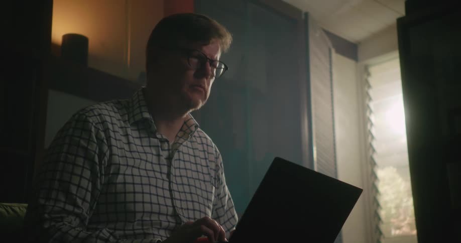 A man feverishly types on his laptop stopping briefly to think