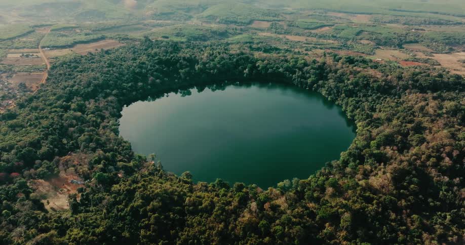 A small circular body of water surrounded by lots of trees and dirt roads is shown in a desolate area