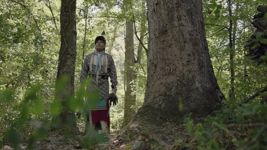 A native american man stands among the trees