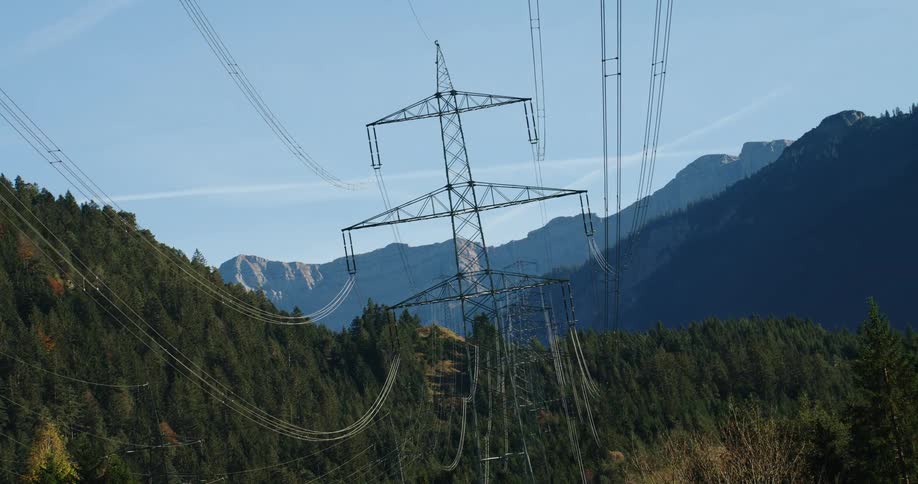 Power lines stretch across electrical wire towers in forested mountains