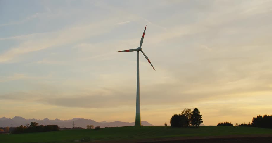 Wind turbine rotates slowly with red sky and misty mountains in the background