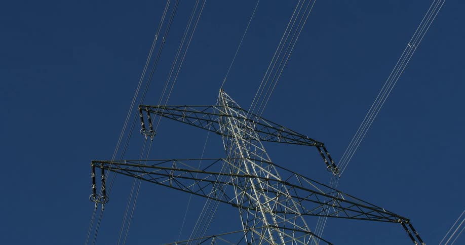 Large electric transmission tower stands under blue sky near mountain