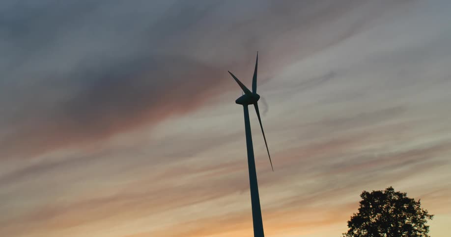 Twisting footage of a wind turbine spinning on the countryside at evening