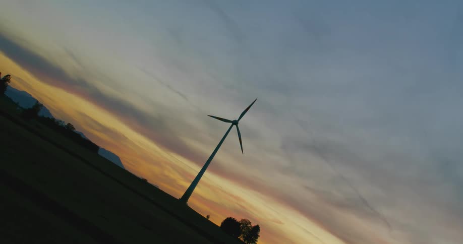 Twisting footage of a wind turbine spinning on the countryside at evening