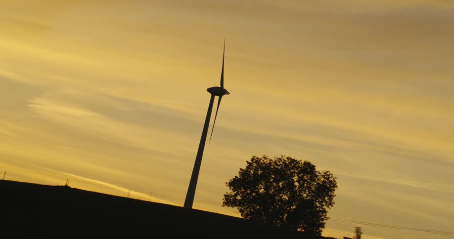 Twisting footage of a wind turbine spinning on the countryside at evening
