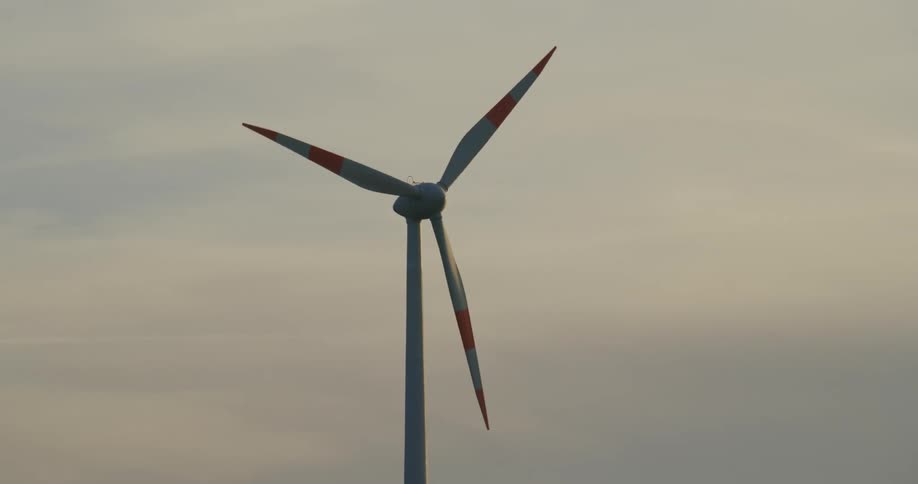 Wind turbine with striped blades rotates slowly under an overcast sky