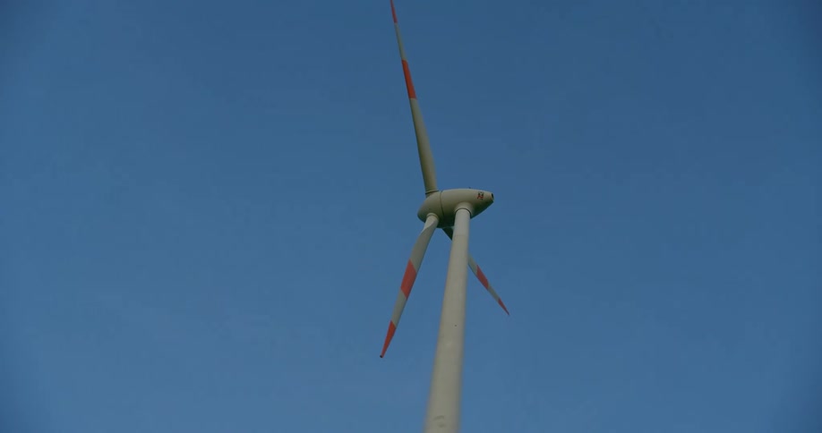 Wind turbine with rotating striped blades stands under blue sky