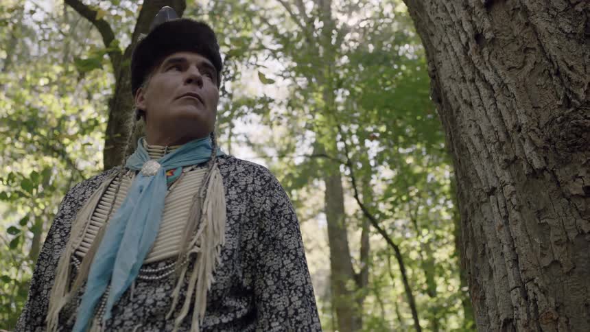 A standing native american man with leaves blowing behind him