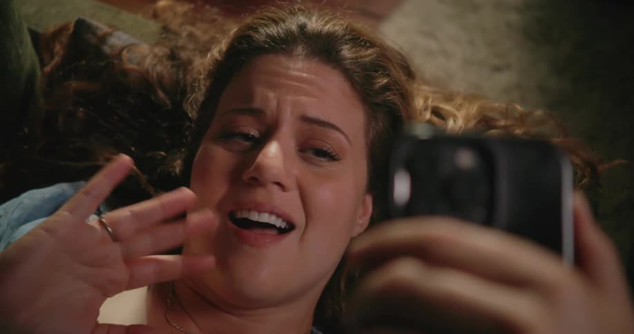 Woman reclining on couch waves at phone while making a video call