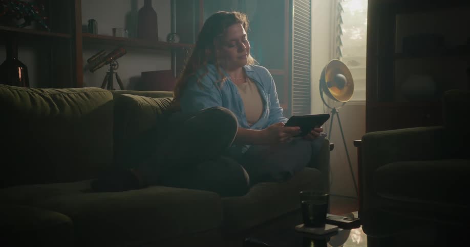 A woman is sitting on the couch in her living room relaxing as she browses online