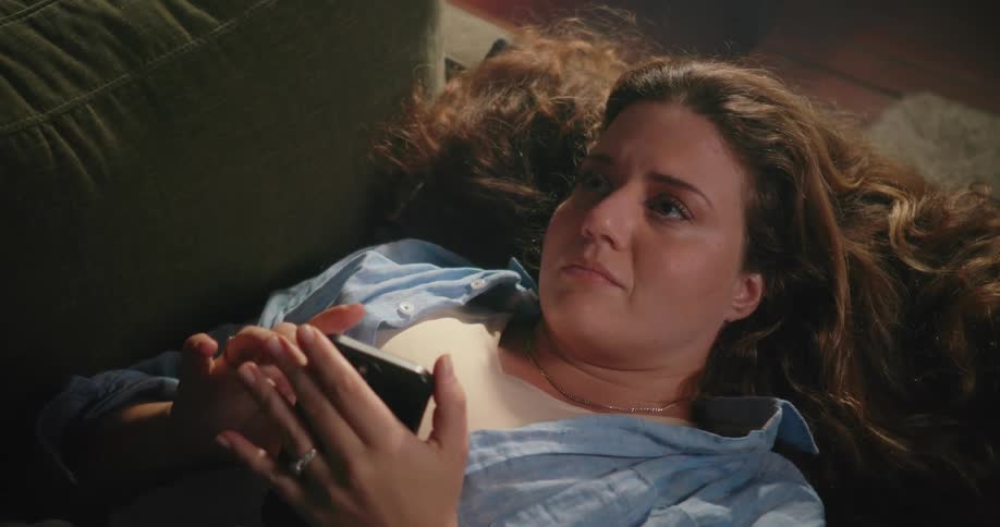 A woman looks through her phone while lying on the couch