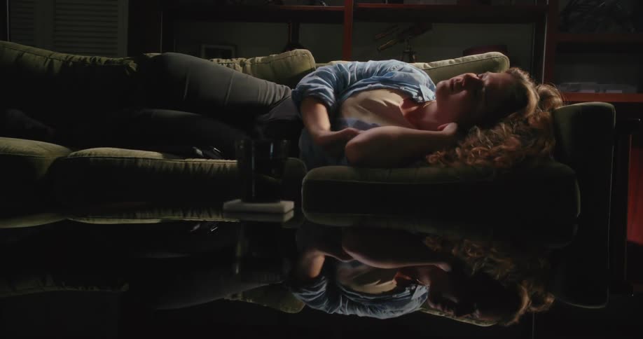 Woman sleeps on couch near reflective coffee table