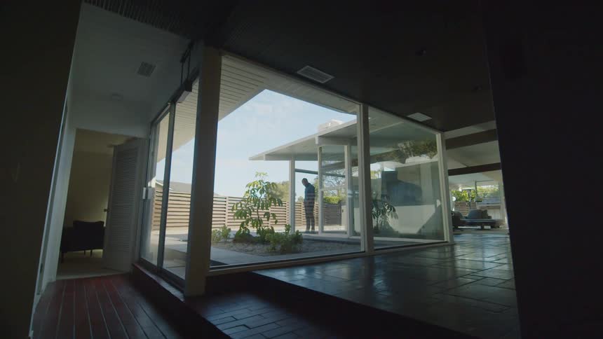 A man stands in a house and looks out the window in to the yard
