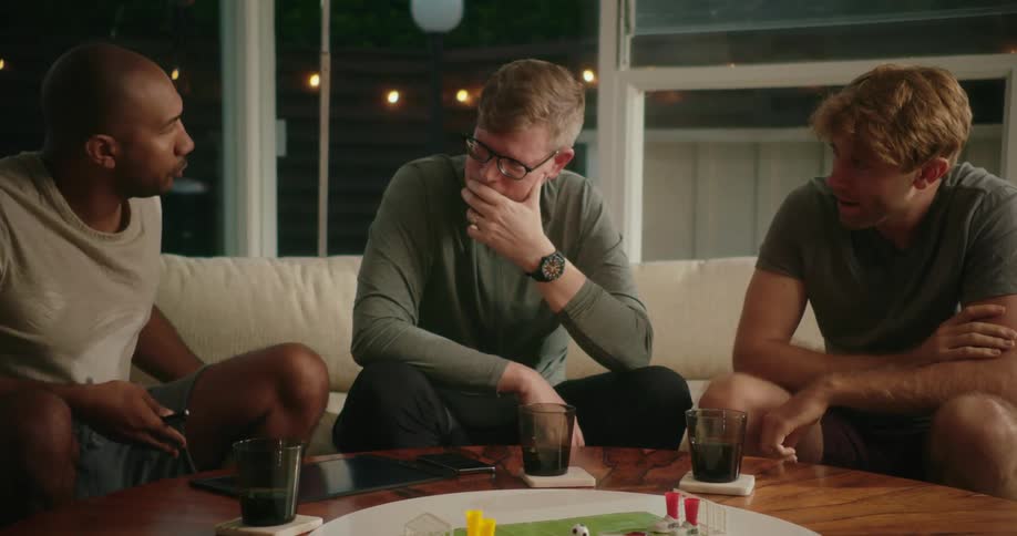 Three men laugh while playing a board game at home