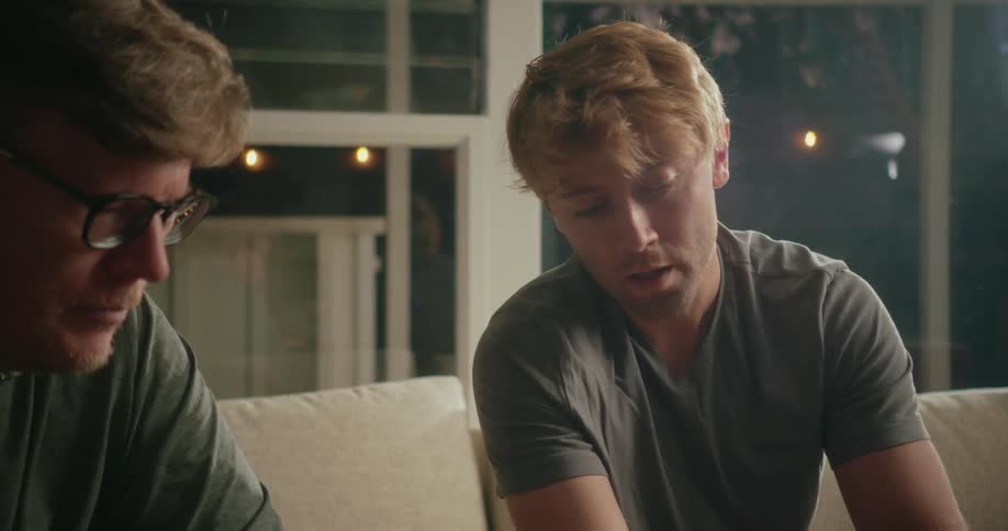 A young man is sitting on the living room couch speaking to his father