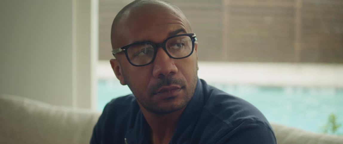 Young bald man wearing glasses sits on the couch at home near the pool