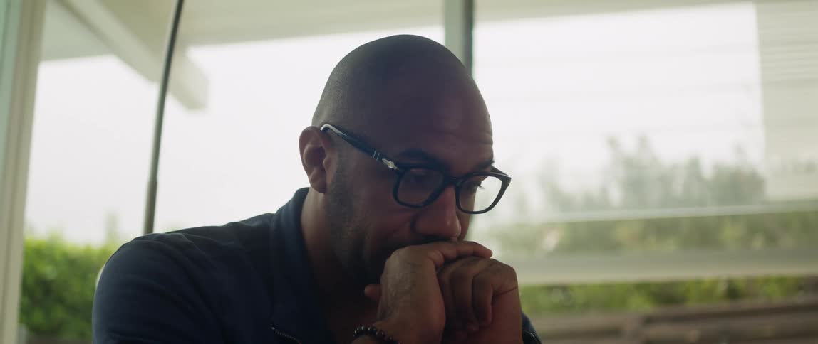 A man is sitting down next to a window during midday