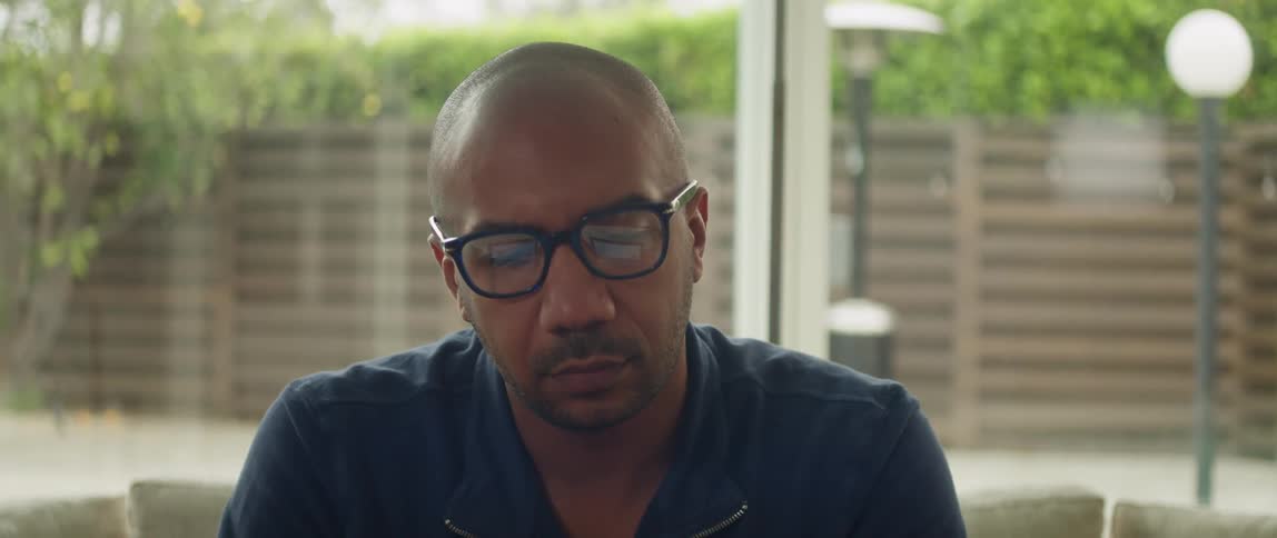 A man wearing glasses deep in thought on a living room sofa