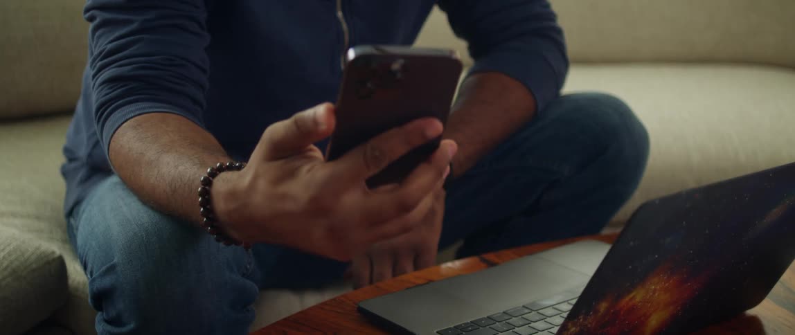 A man is sitting on a couch with his electronics