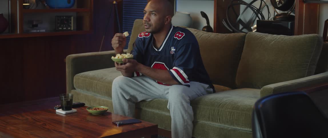 Young man sitting on a couch at home watching sports while holding a snack bowl in his hands
