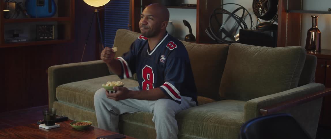 A man is sitting on a couch and watching a sports game