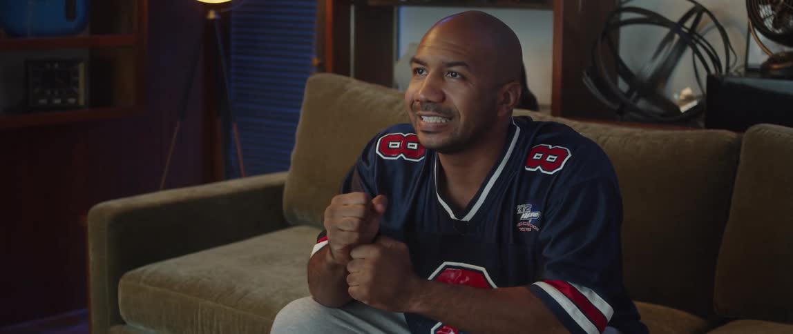 A man sits on a couch while excitedly watching sports while snacking