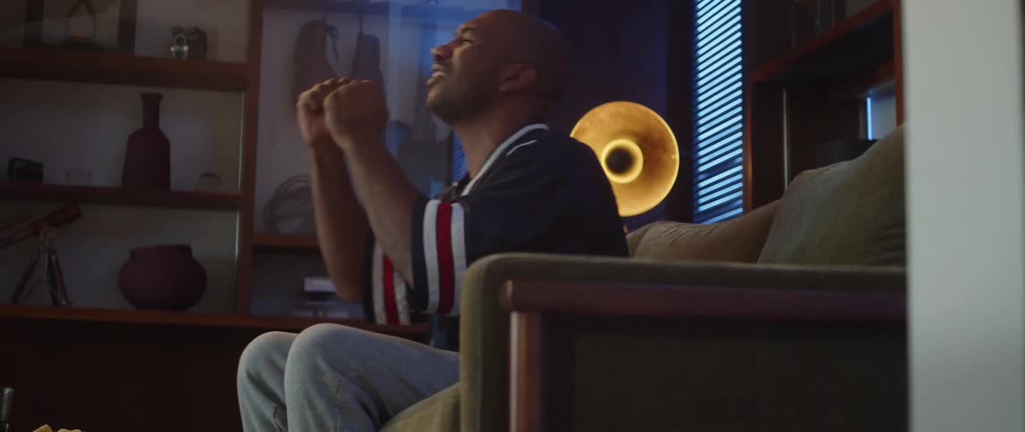 A man yells while sitting on the couch and watching sports