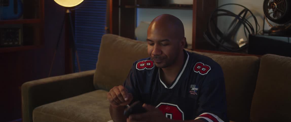 A man sits on a couch at home and talks on the phone and then hangs up and happily bumps his fist in the air