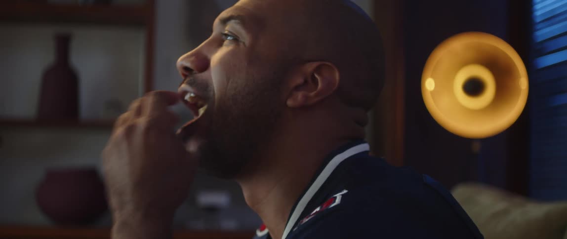 A man cheering while eating chips and watching sports on television