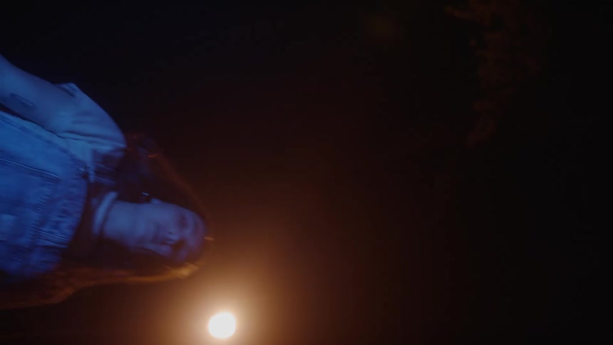 A teenage girl steps in front of a bright flare and bends down