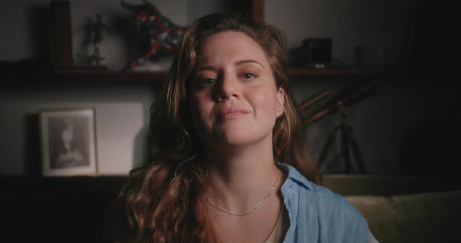 Woman with brown wavy hair and blue shirt smiles at camera in living room