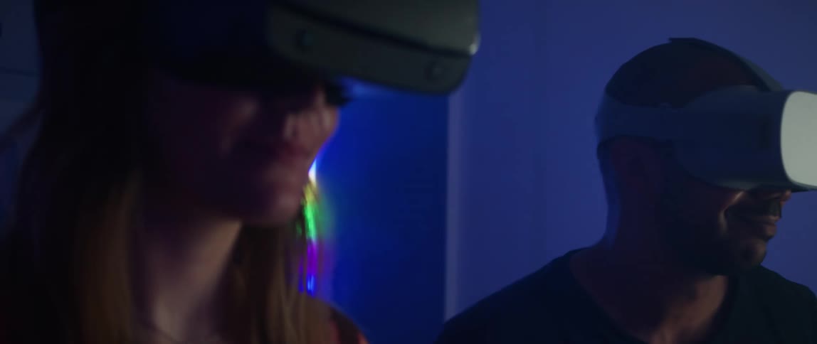 A man and woman smile as they both put on a virtual reality headset