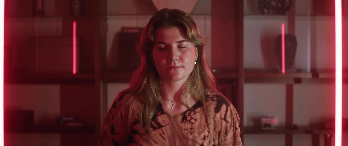 Close up of the face of a woman looking at the camera standing in a room surrounded by red lights
