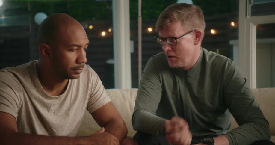 Three men sit on a couch in a home and talk together and one man writes something down