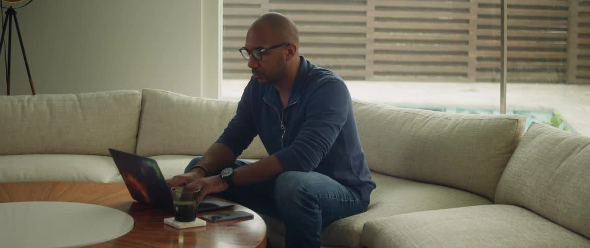 Young bald man wearing glasses working on a laptop in the living room near a pool